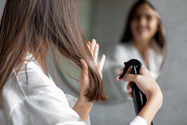 A woman spraying her hair with a spray bottle.
