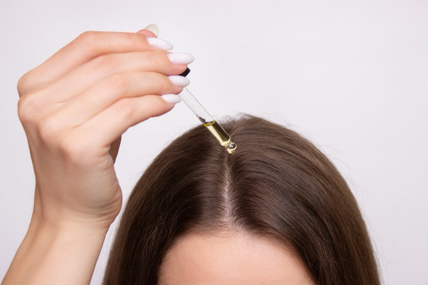 A person applying oil to their hair with a dropper.