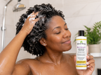 Woman washing hair while holding Little Miracles shampoo bottle